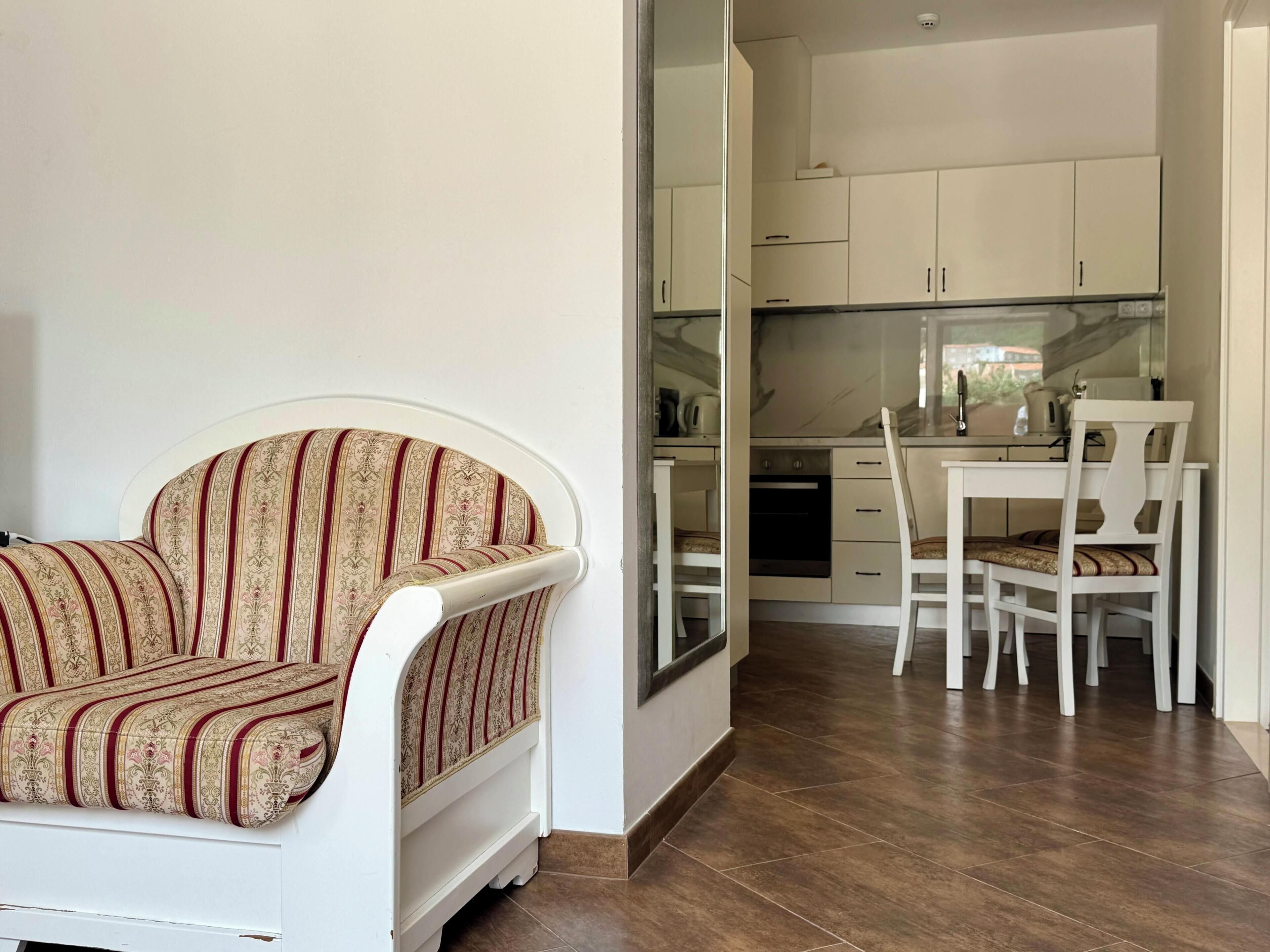 Een kamer met een bank, een eettafel met stoelen, een keukenhoek met kastjes en een inbouwoven.