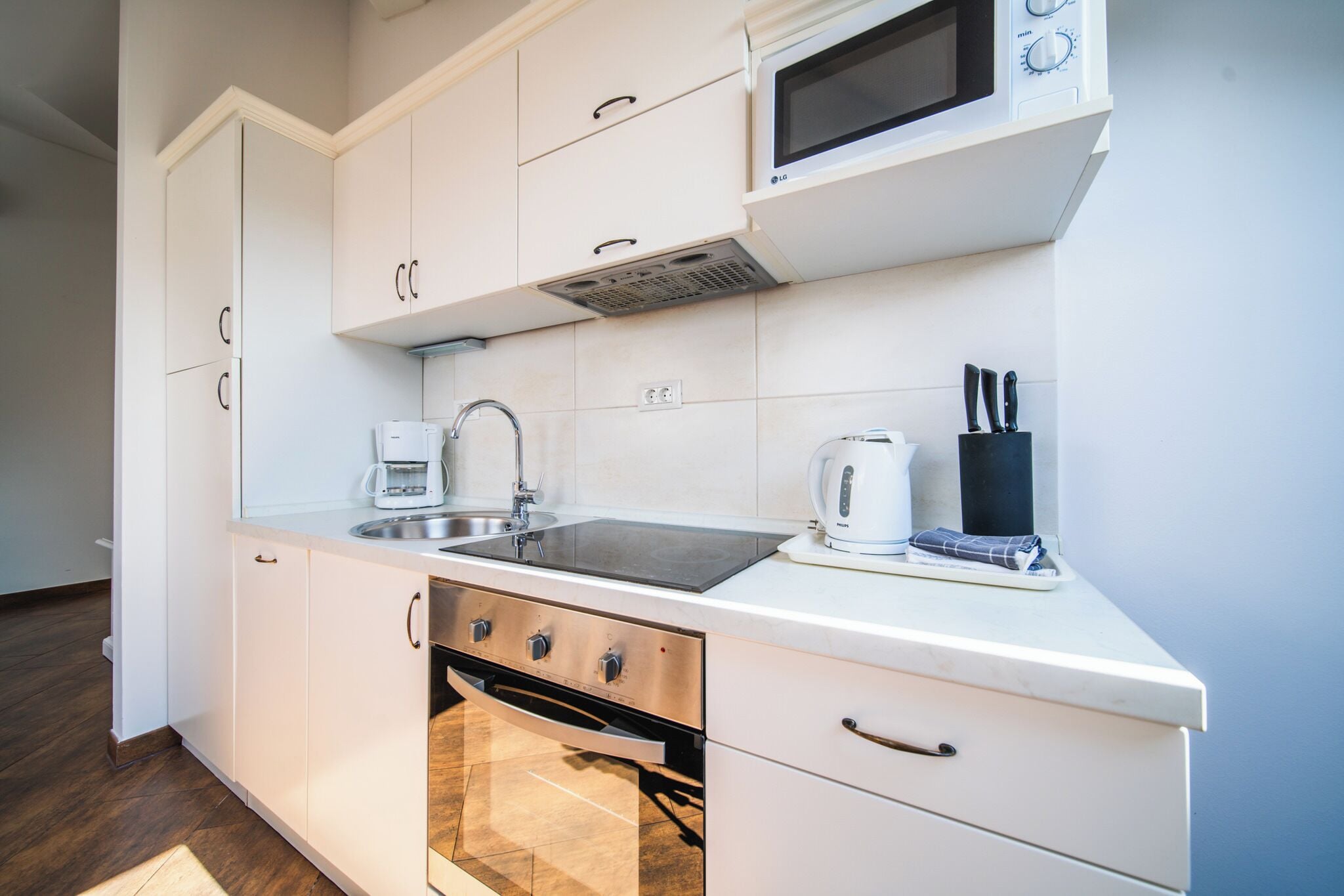A modern kitchen with white cabinets, a stainless steel sink, a microwave, and a built-in oven.