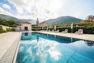 Una piscina con sillas de descanso, un edificio pequeño y una iglesia al fondo.