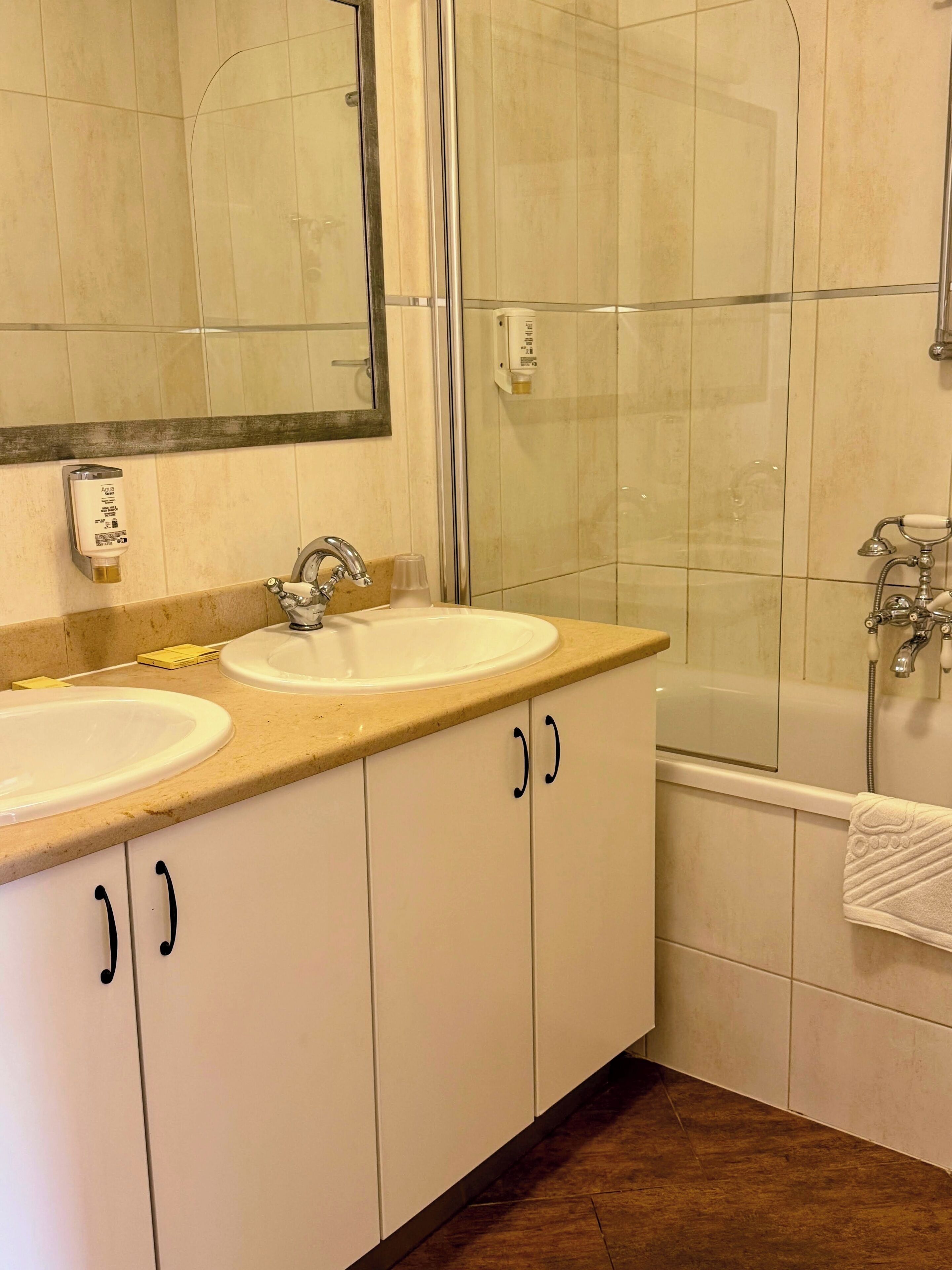 A bathroom with two sinks, a mirror, a glass shower enclosure, and a bathtub.