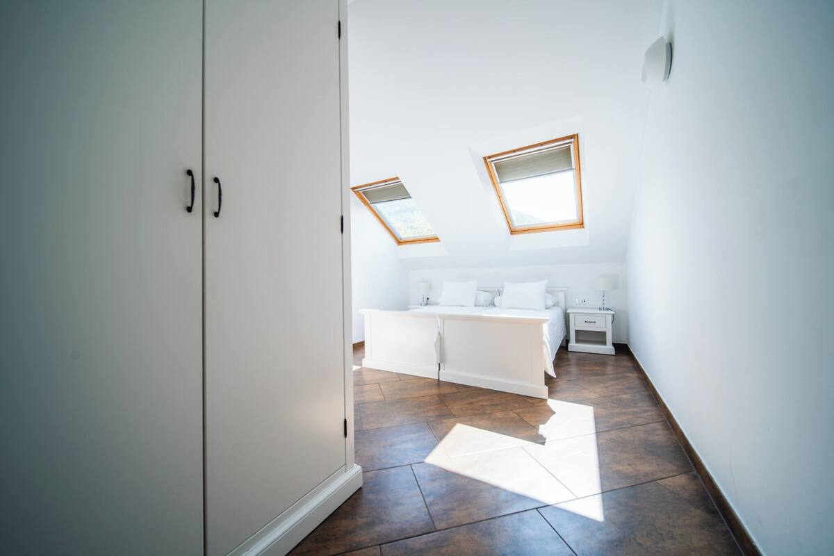 A bedroom with a bed, bedside tables, and a wardrobe. There are skylights above the bed.