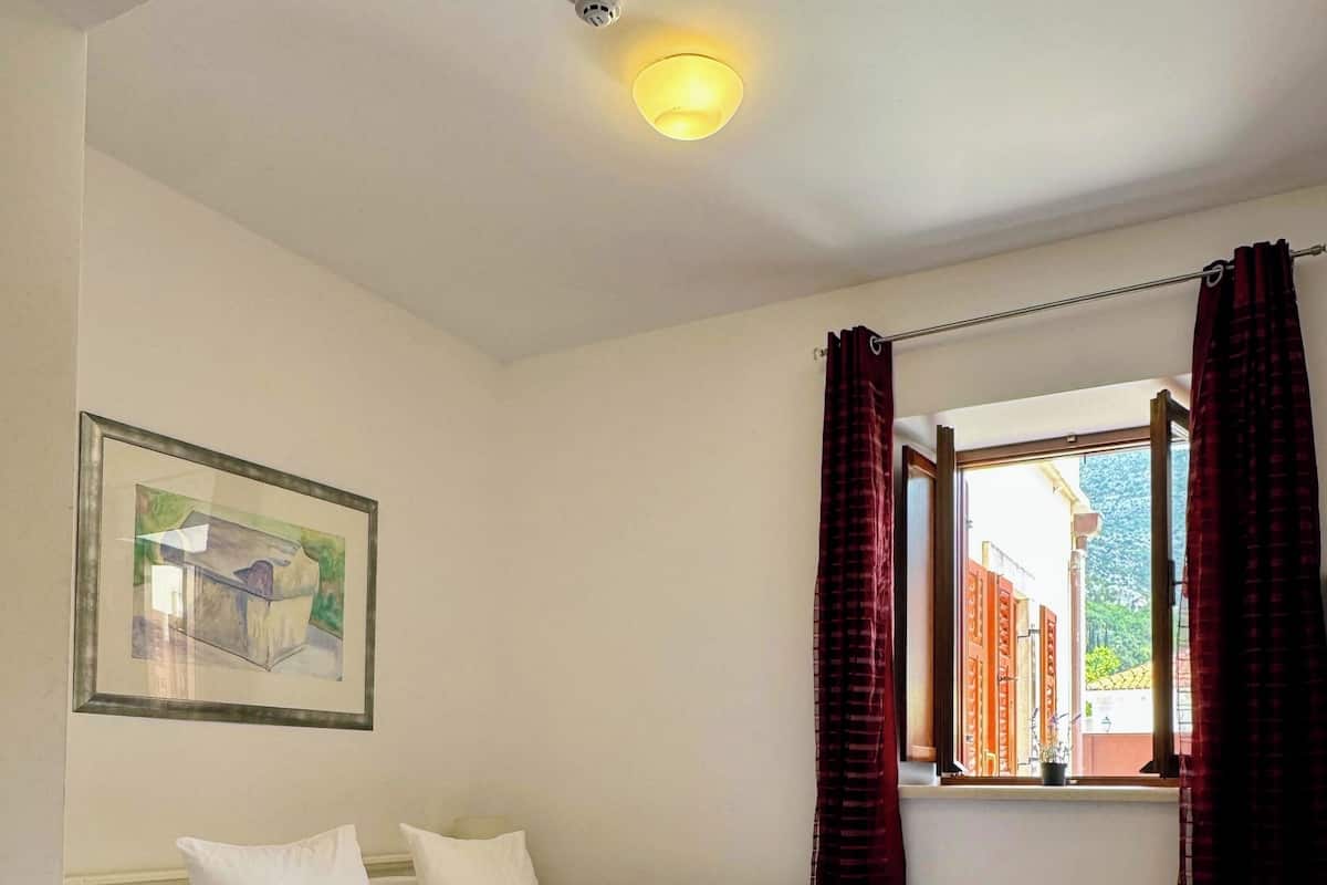 A bedroom with a bed, a window with curtains, a ceiling light, and a framed picture on the wall.