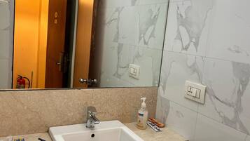 A bathroom with a white sink, a mirror, and marble walls.