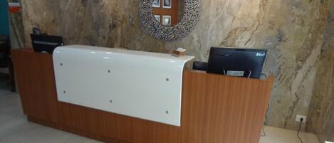 Un mostrador de recepción con una pared de mármol al fondo, un espejo decorativo y un monitor de computadora sobre el mostrador.