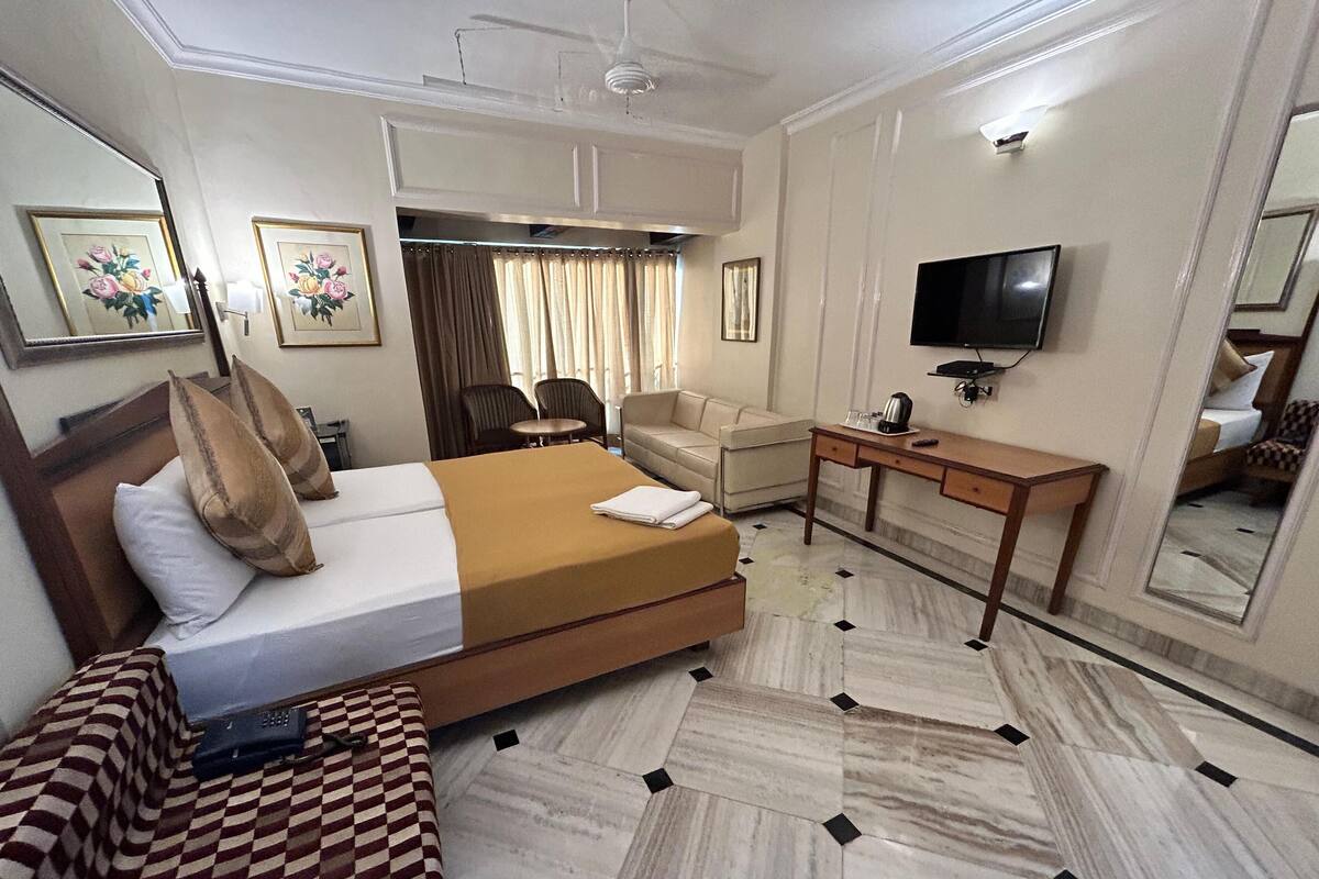 A hotel room with a bed, a desk, a chair, a television, and a mirror.