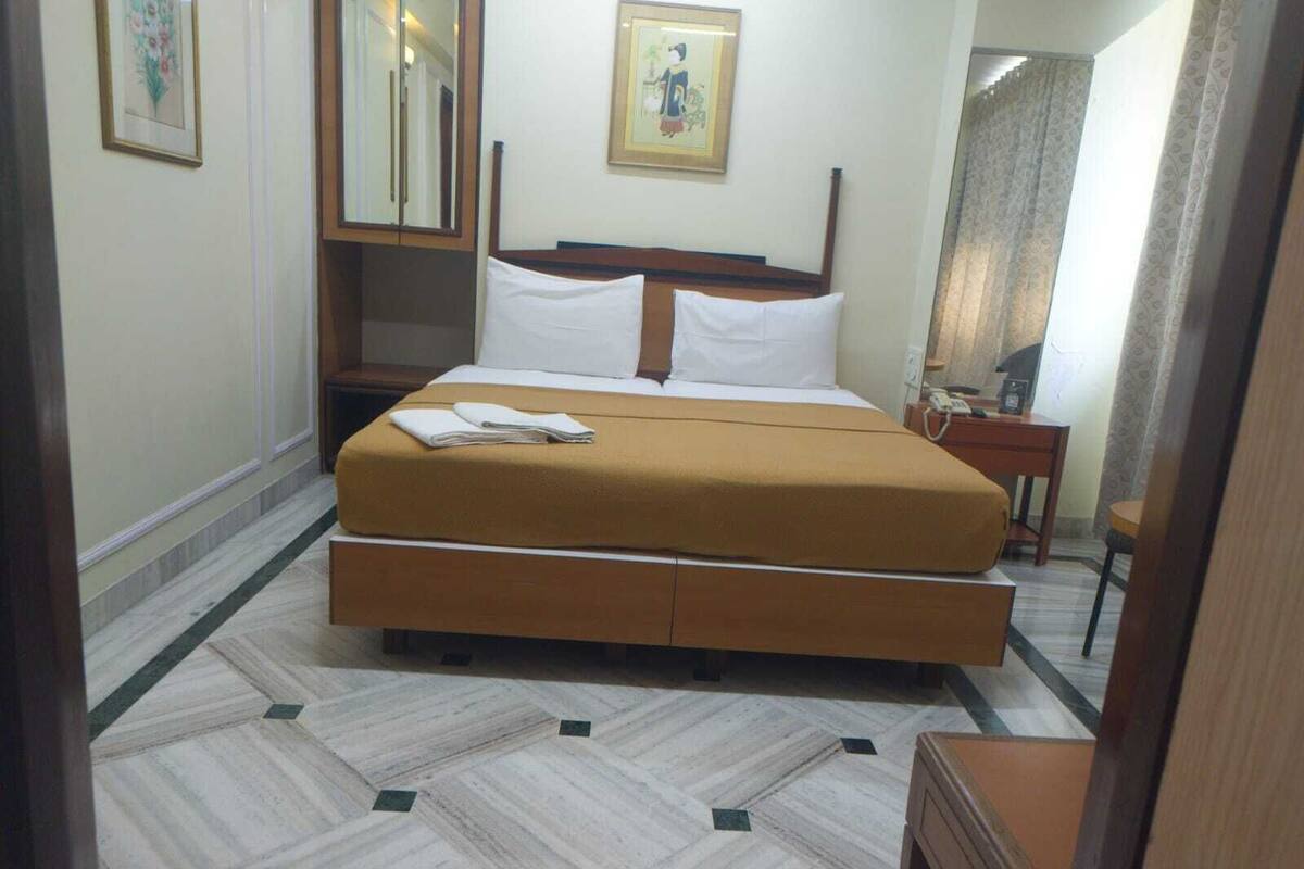 A hotel room with a large bed, a bedside table, a mirror, and a framed picture on the wall.