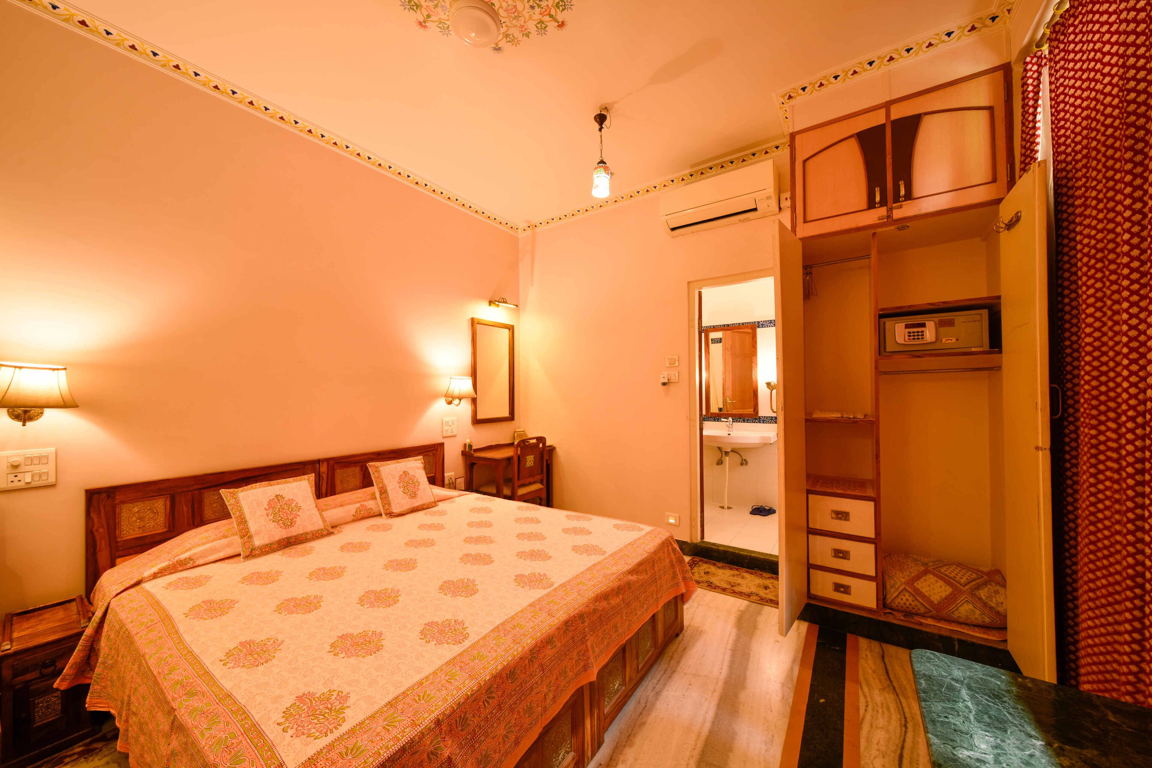 Camera d'albergo con un letto grande, un armadio, uno specchio e un bagno piccolo visibile attraverso una porta aperta.
