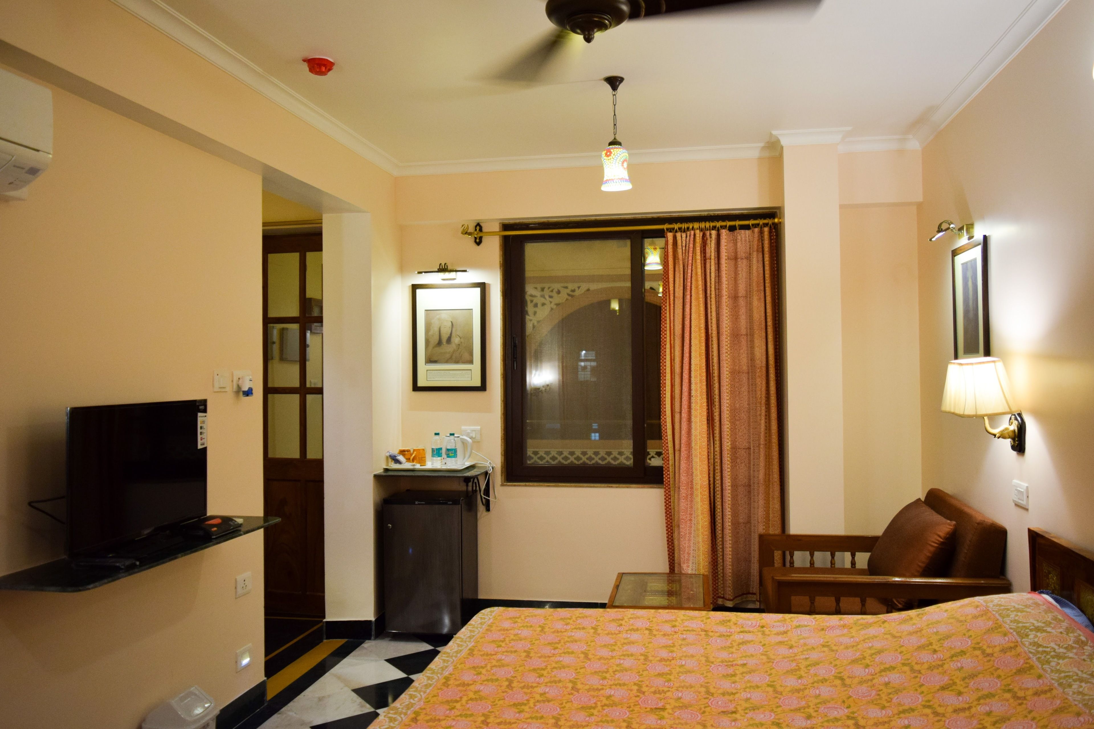 A hotel room with a bed, a TV, a desk, a chair, and a window with curtains.