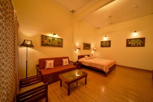 Quarto com piso de madeira, um sofá, uma cama, uma mesa com tampo de vidro e luminárias fixadas na parede.