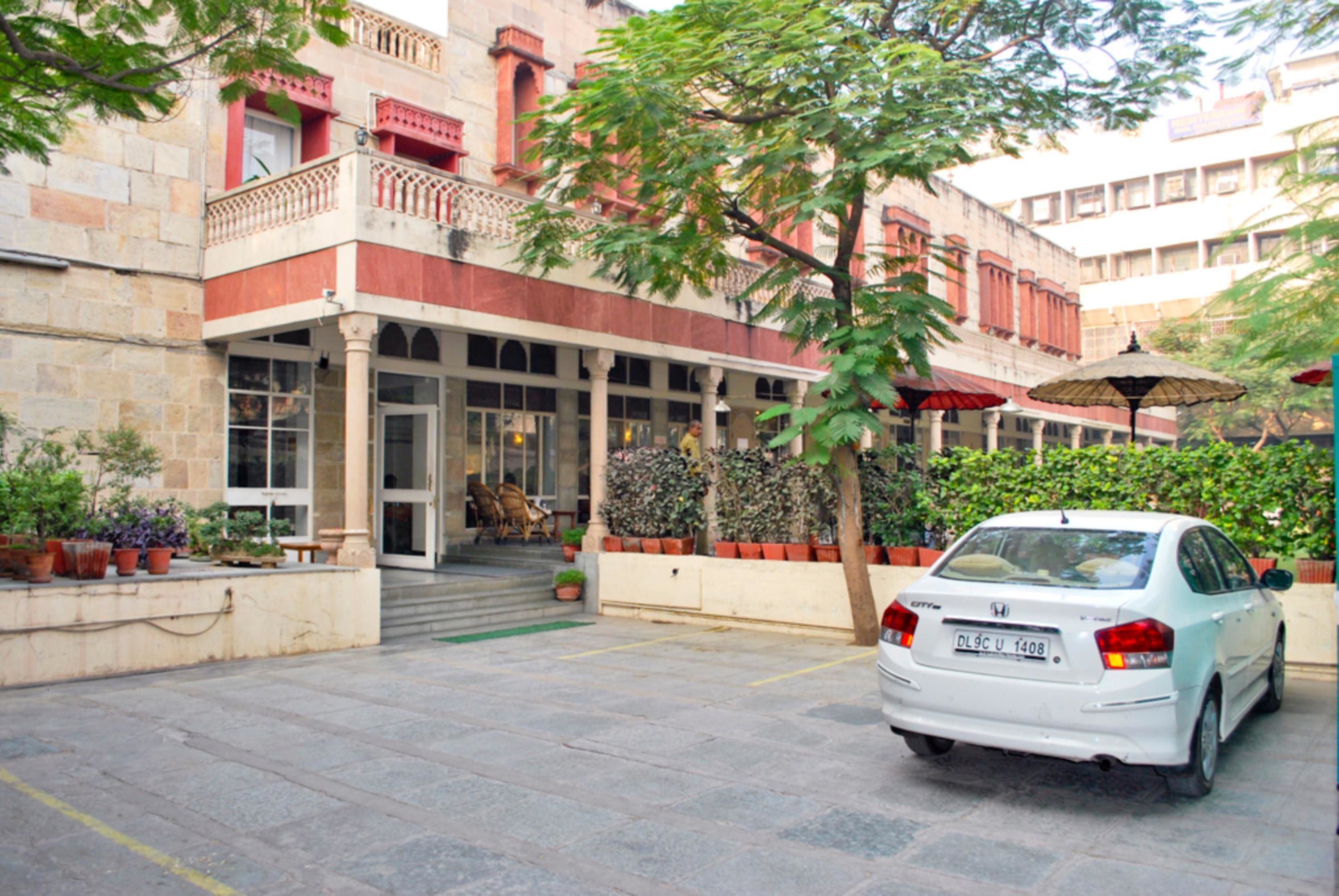 A white car parked in front of a building with a red and beige facade, large windows, and a balcony.
