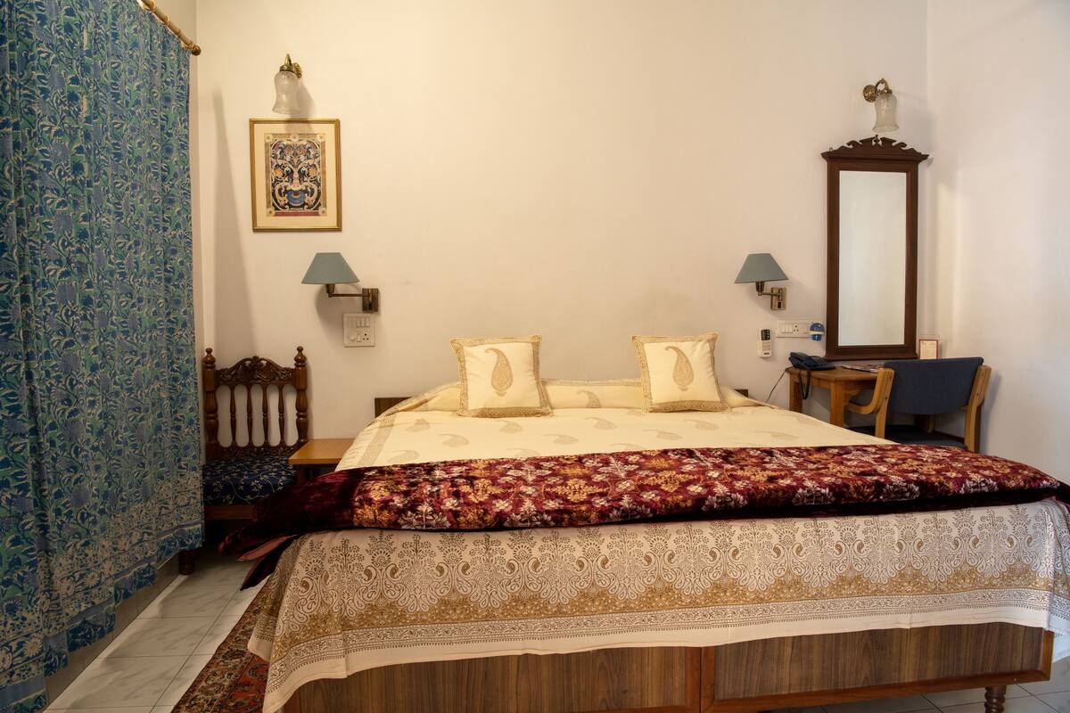 Un dormitorio con cama, una silla, escritorio, espejo y lámpara.