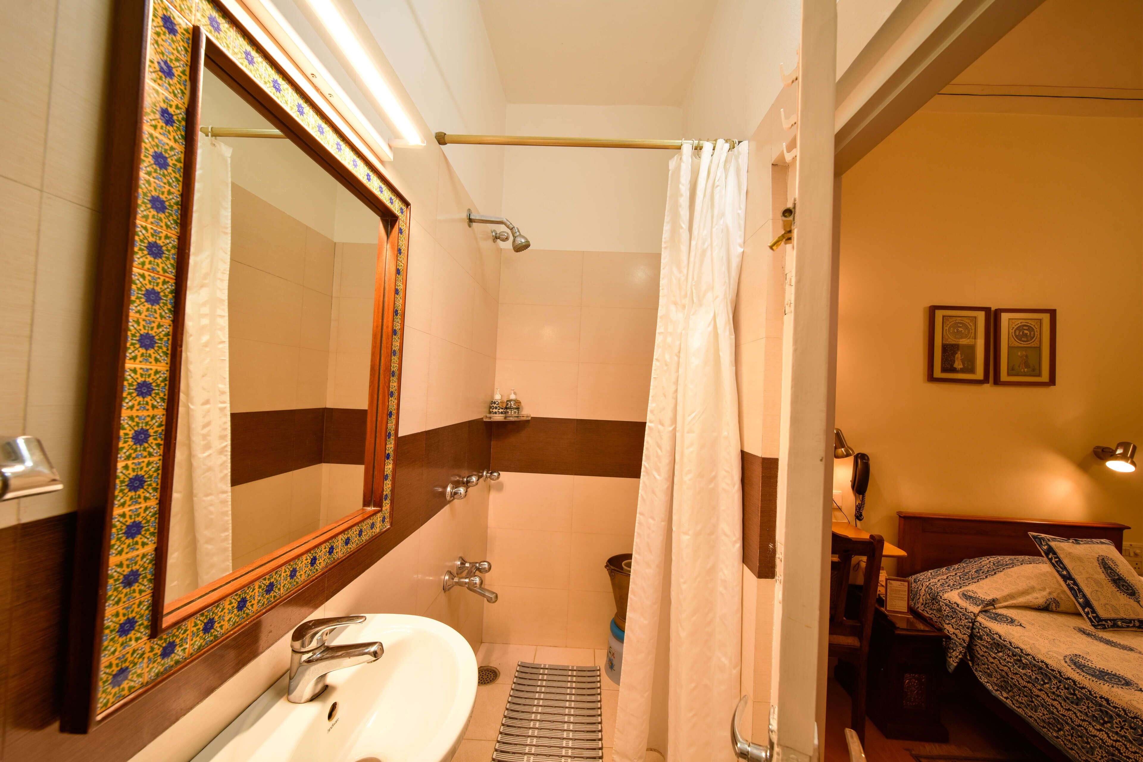A bathroom with a sink, mirror, shower, and a bed with a nightstand.