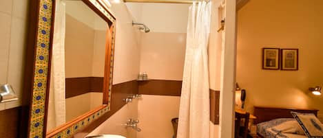 A bathroom with a sink, mirror, shower, and a bed with a nightstand.