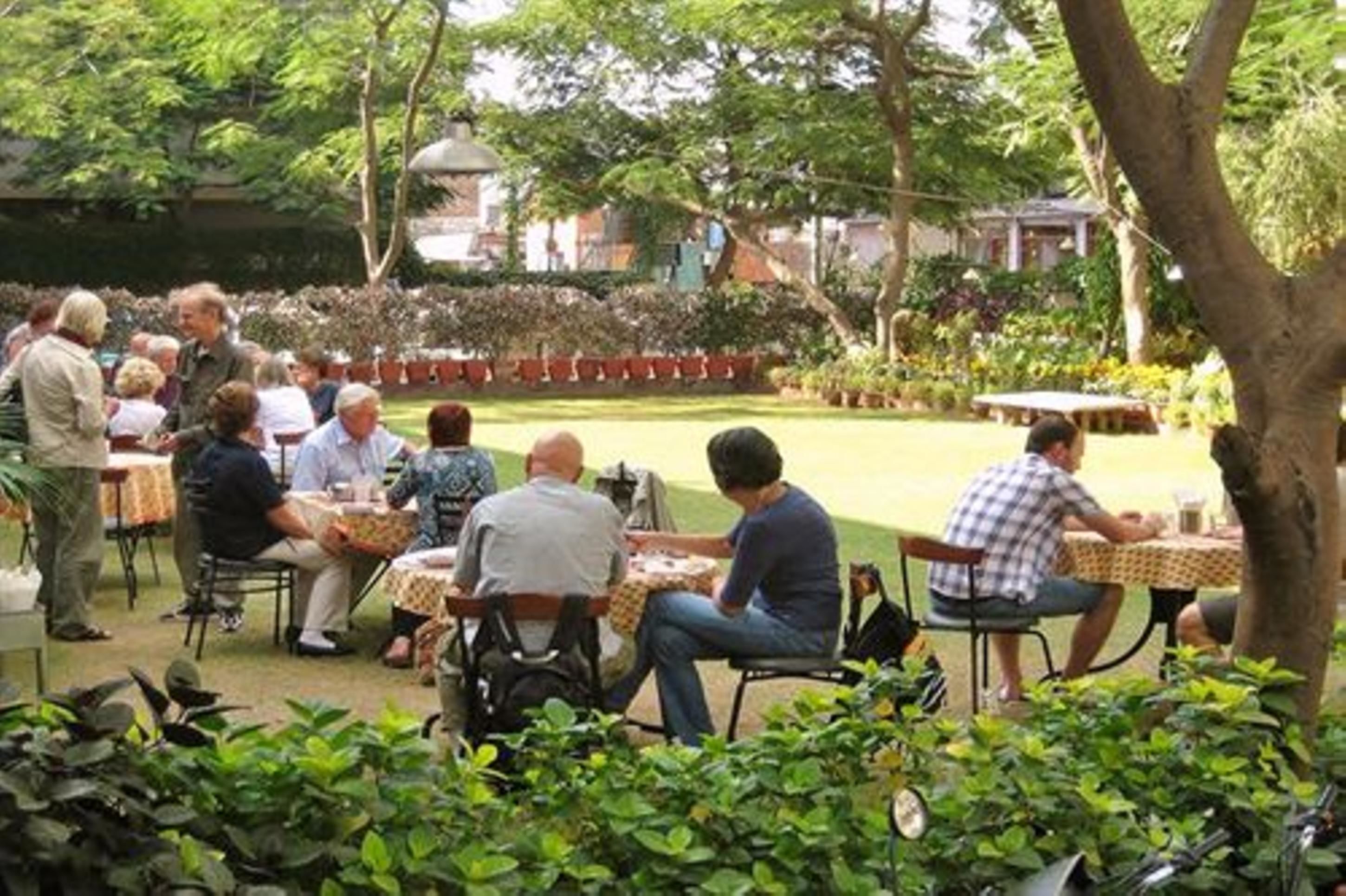 Ein Garten mit Terrassentischen und -stühlen, umgeben von üppigem Grün und Pflanzkübeln.