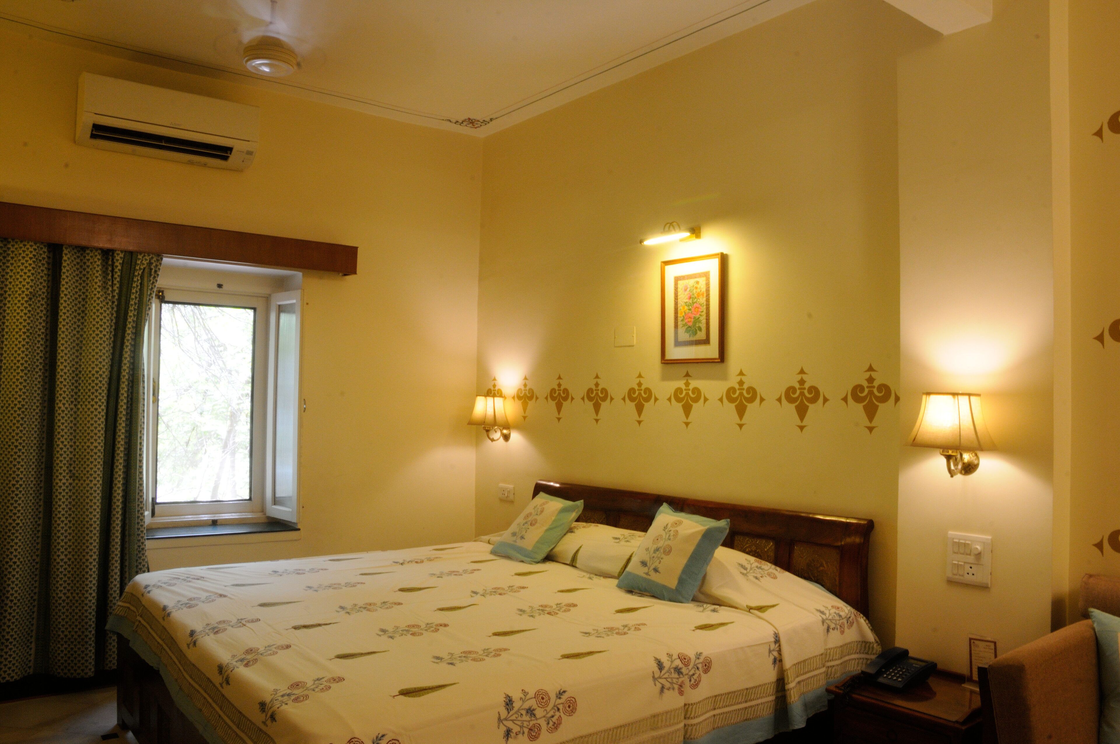 A hotel room with a bed, a window with curtains, wall-mounted lamps, and a framed picture on the wall.