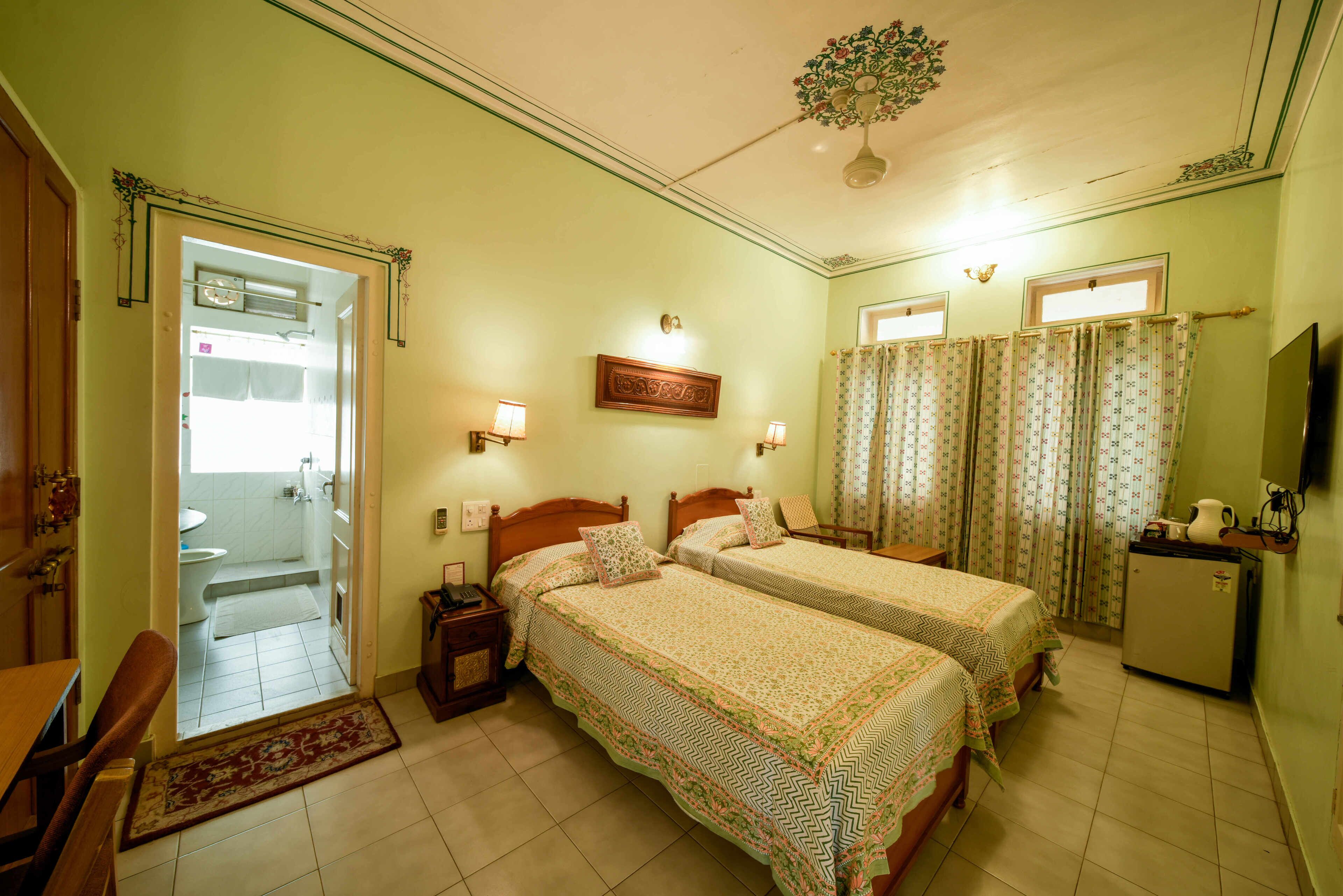 A bedroom with two beds, a desk, a chair, a small refrigerator, and a television.