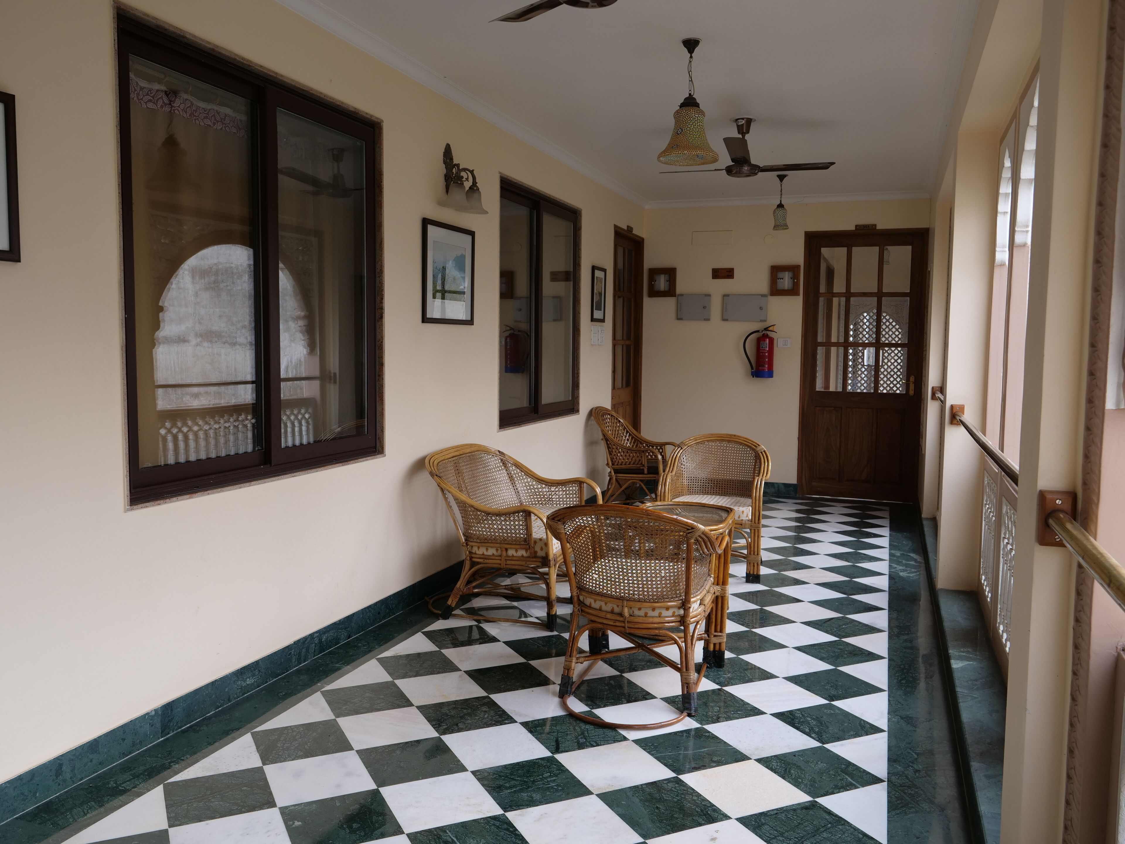 A corridor with checkered flooring, wicker chairs, ceiling fans, and framed pictures on the walls.