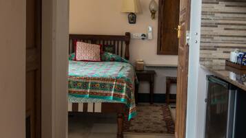 Una habitación con cama, una mesita, una lámpara y una zona de cocina con refrigerador.