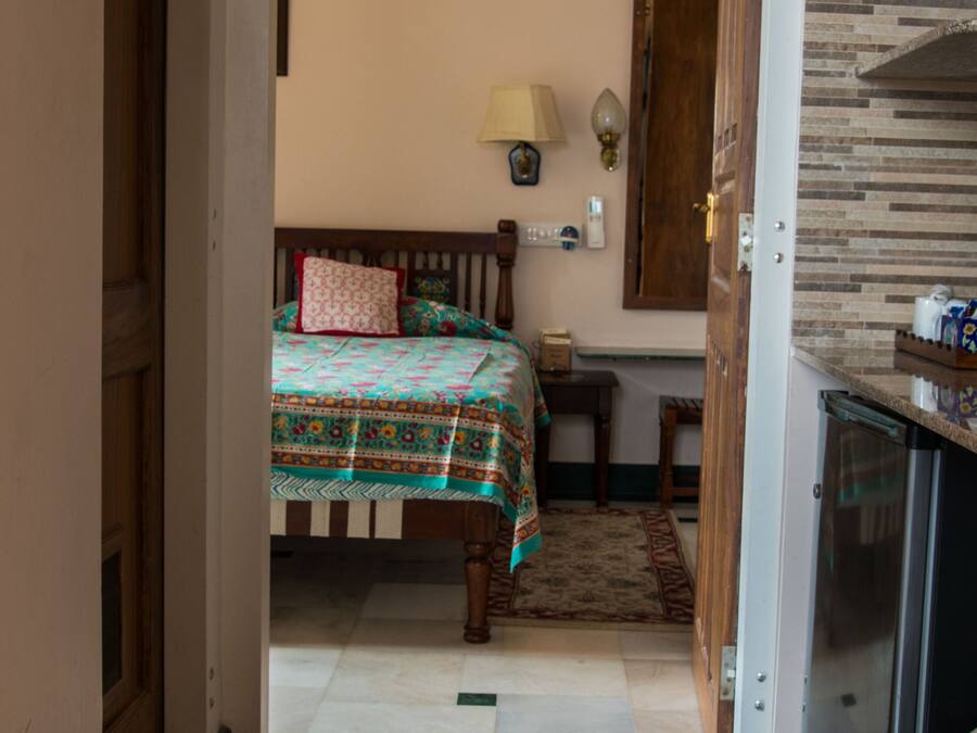 Una habitación con cama, una mesita, una lámpara y una zona de cocina con refrigerador.