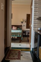 Quarto com cama, mesa pequena, luminária e cozinha equipada com geladeira.