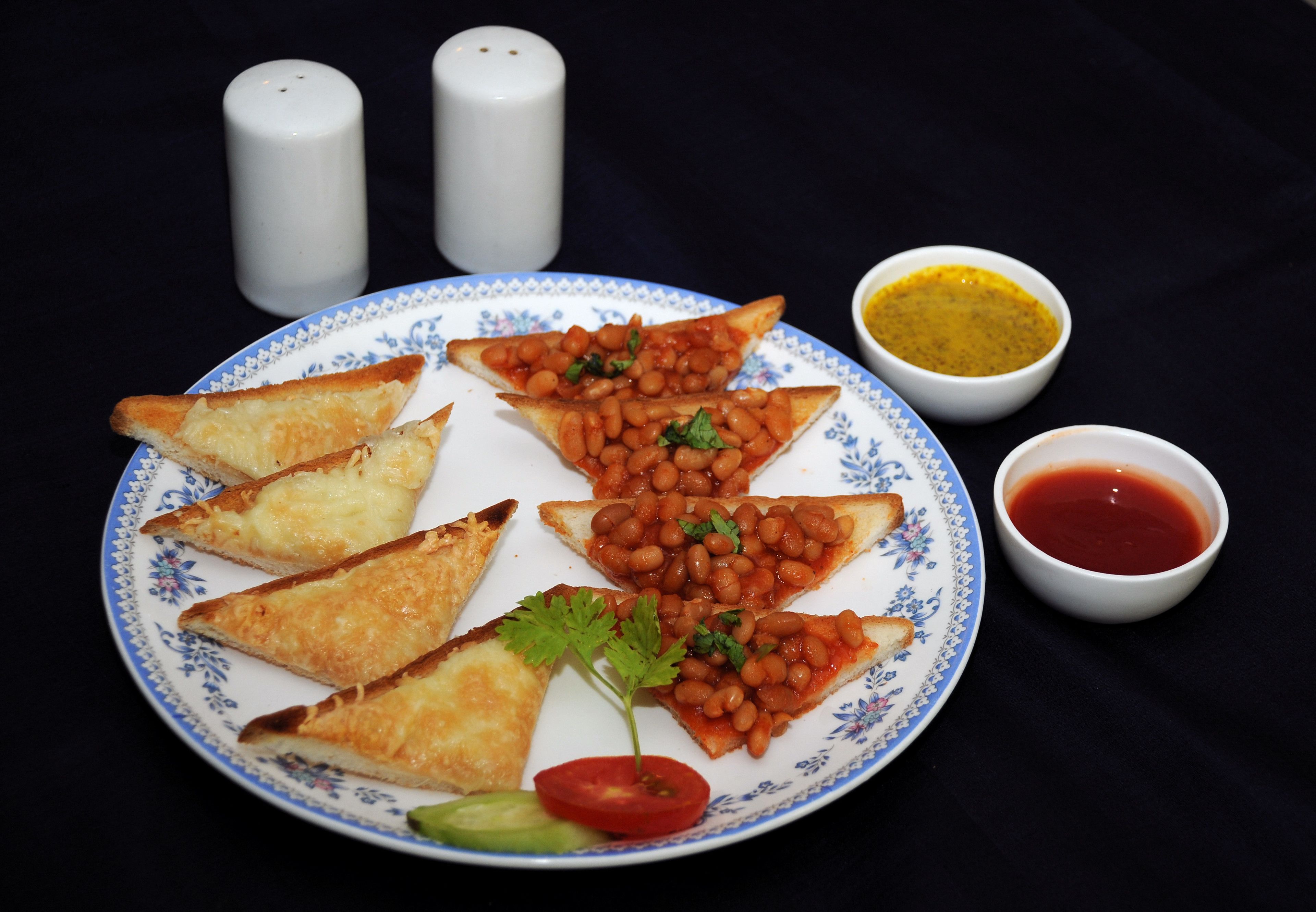 A plate with triangular food items, a small bowl of sauce, and two salt shakers.