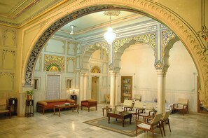 A spacious lobby with ornate arches, a central seating area, and a chandelier. - Arya Niwas (Jaipur)
