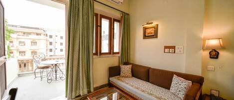 A living room with a sofa, a glass coffee table, a dining table with chairs, and a view of the outside balcony.