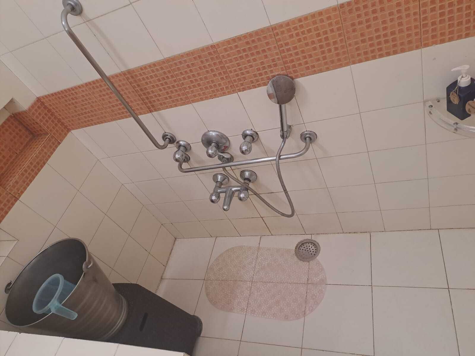 A shower with a handheld showerhead, a wall-mounted faucet, and a floor drain.
