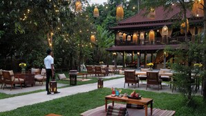 An outdoor seating area with tables and chairs, surrounded by greenery and string lights. - The Community - Siem Reap (Siem Reap)