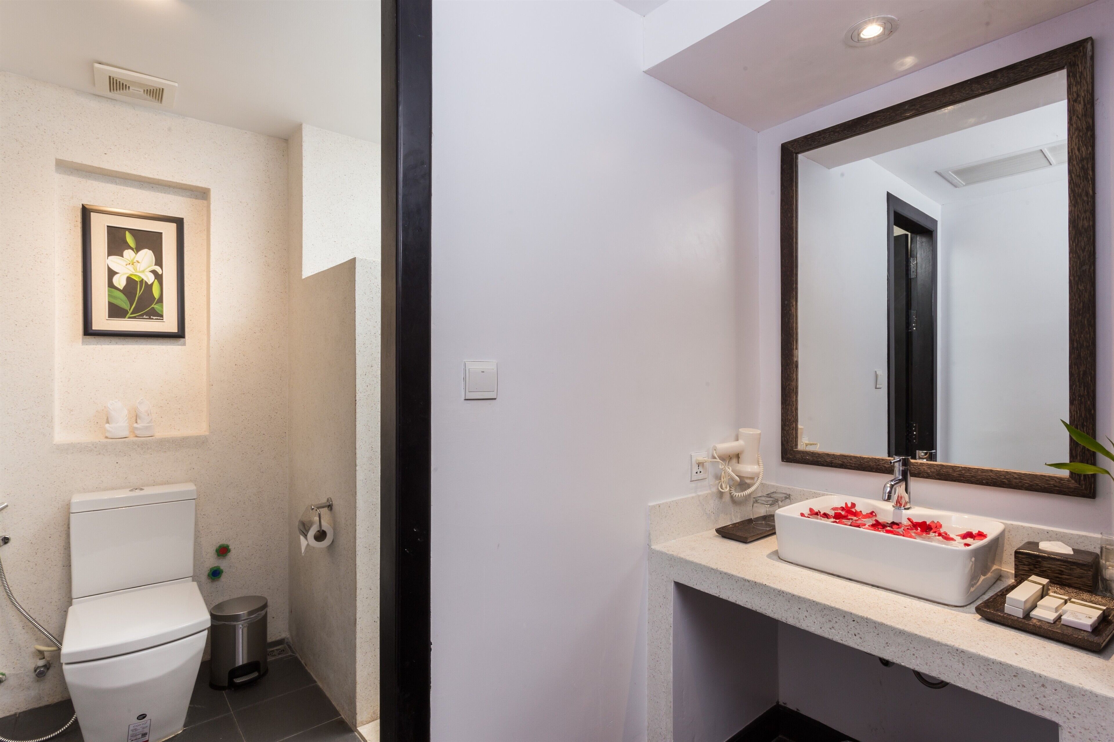 Un baño con inodoro, lavamanos, espejo y un cuadro en la pared.