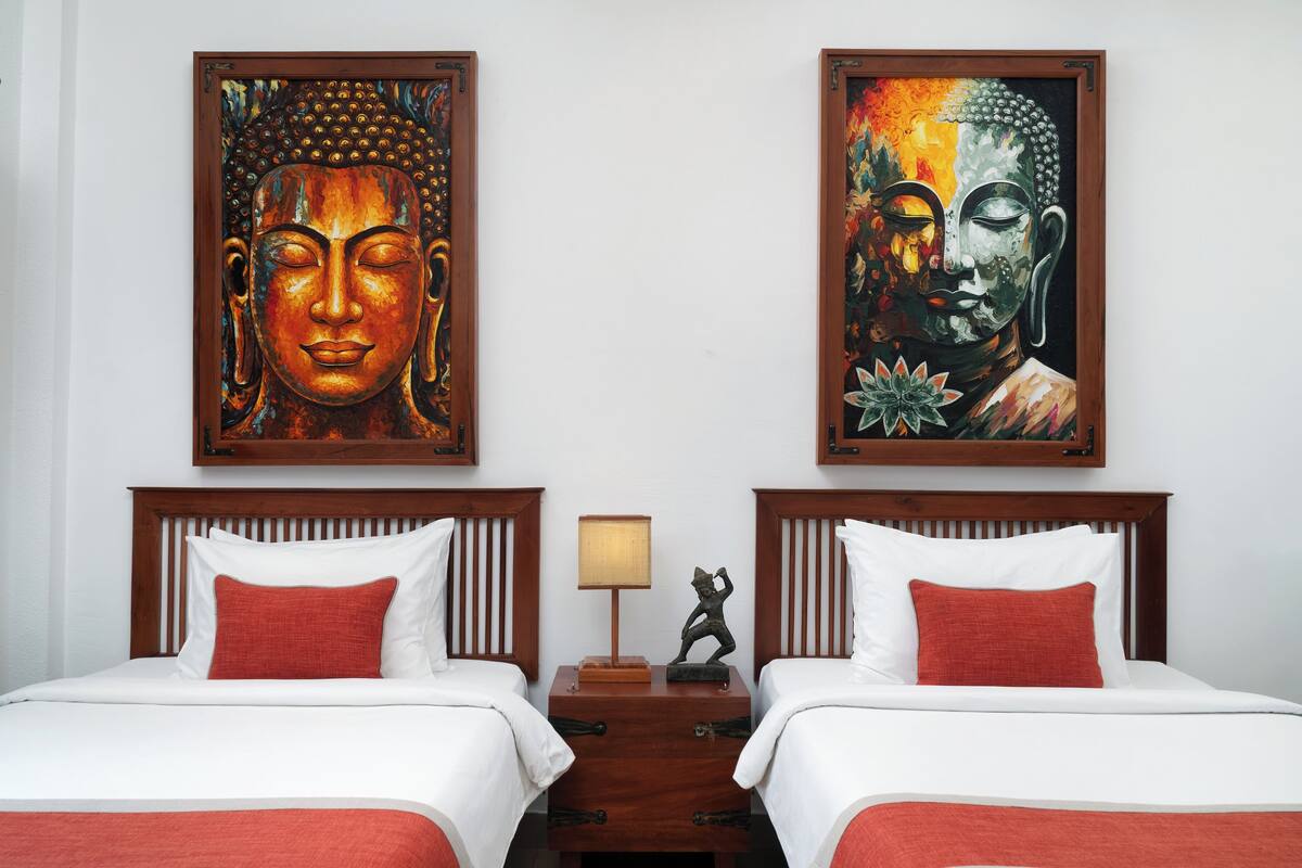 A hotel room with two beds, a nightstand with a lamp, and two Buddha paintings on the wall.