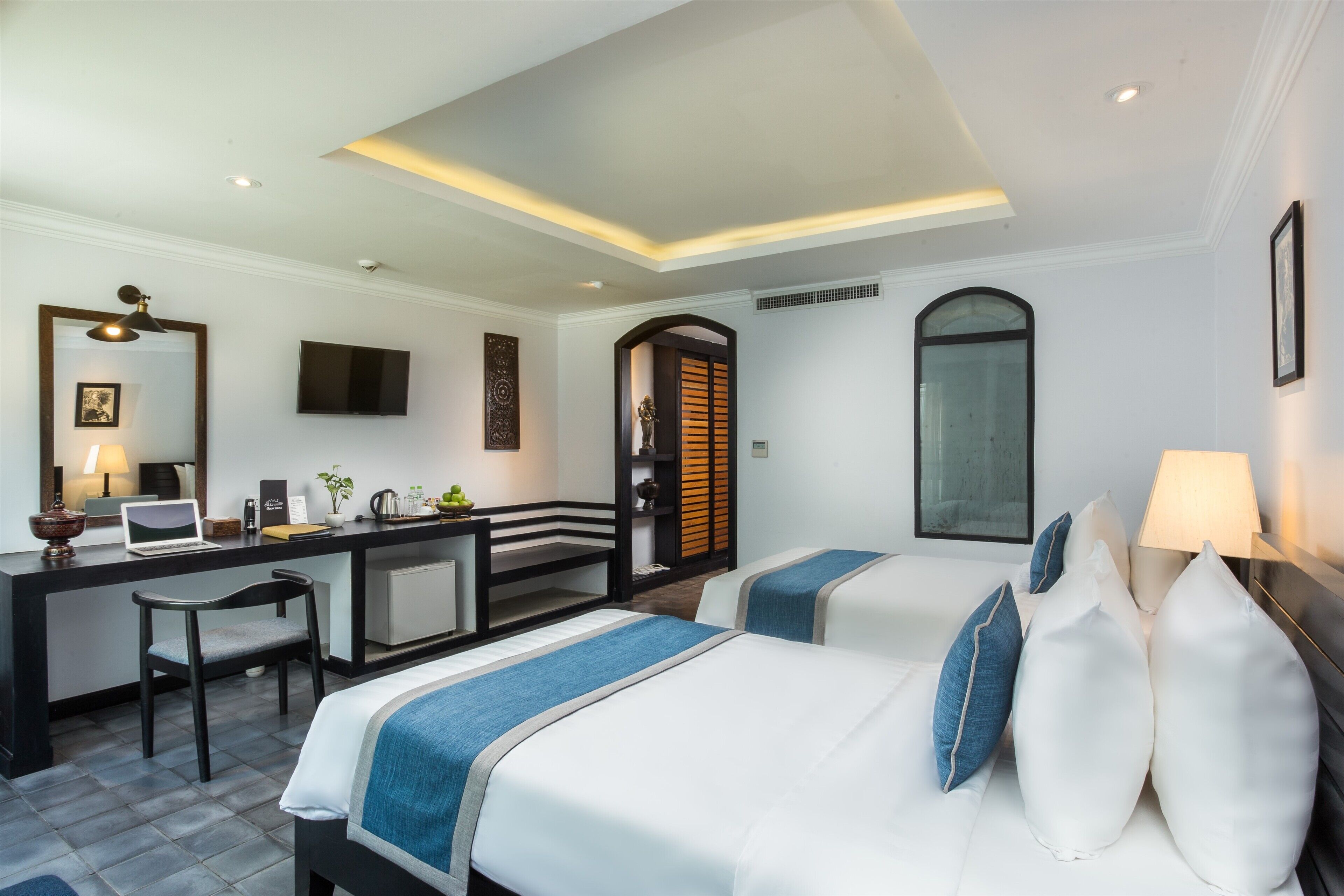 A hotel room with a desk, two beds, a television, and a bathroom with a shower.