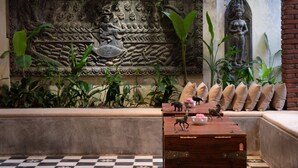 A room with a decorative wall featuring a relief sculpture, a statue, and a checkered floor. - The Community - Siem Reap (Siem Reap)