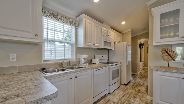 A kitchen with white cabinets, a granite countertop, a microwave, a toaster, and a refrigerator. - Club Naples RV Resort (Naples)