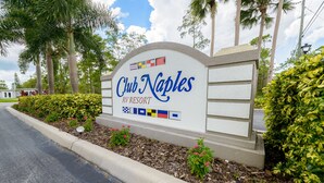 A Club Naples RV Resort sign with a landscaped area and palm trees. - Club Naples RV Resort (Naples)
