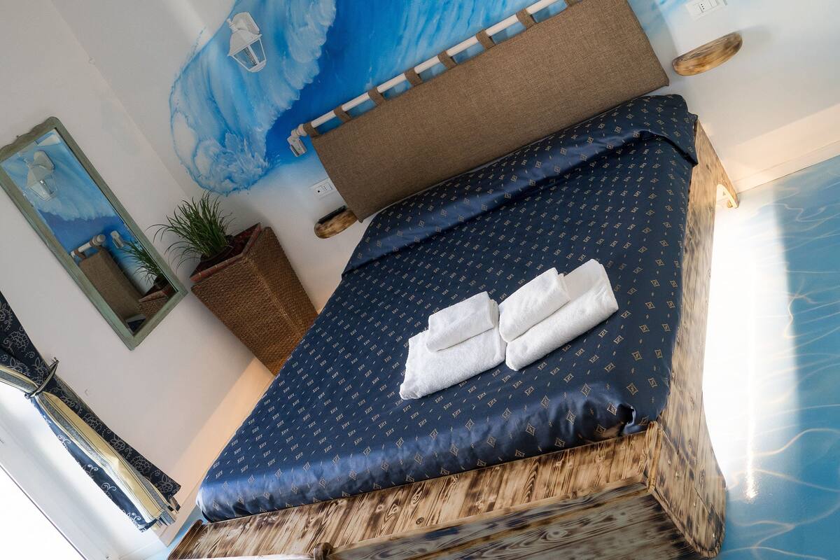 A bed with a blue wave design on the ceiling, a wooden headboard, and a dark blue bedspread with a pattern.