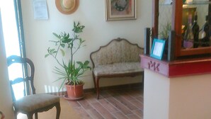 A room with a wooden floor, a chair, a sofa, a potted plant, a hat on the wall, and a painting. - Soggiorno Sogna Firenze (Florence)