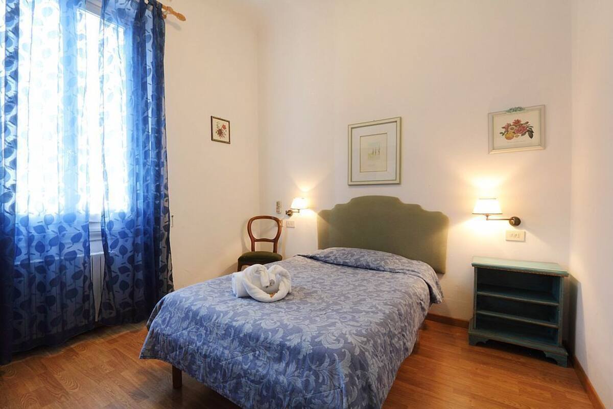 A bedroom with a bed, a chair, a nightstand, and a window with curtains.