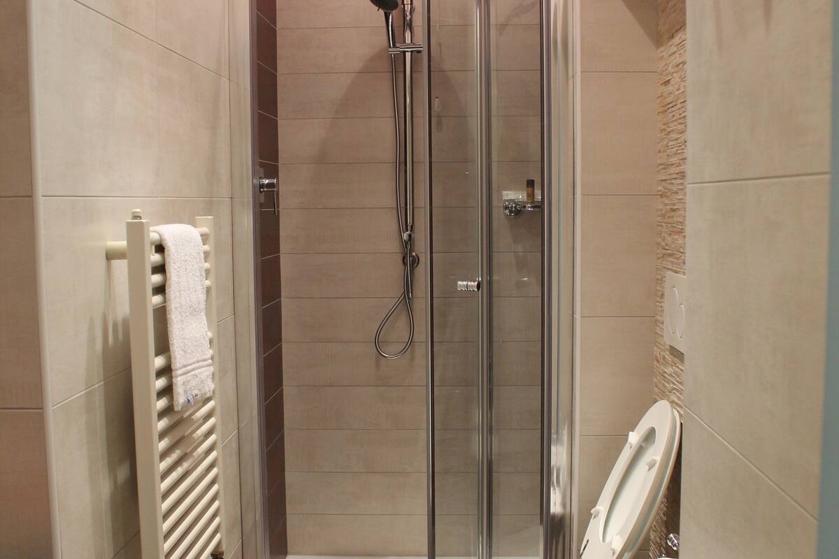 A modern bathroom with a glass-enclosed shower, two toilets, and a towel rack.