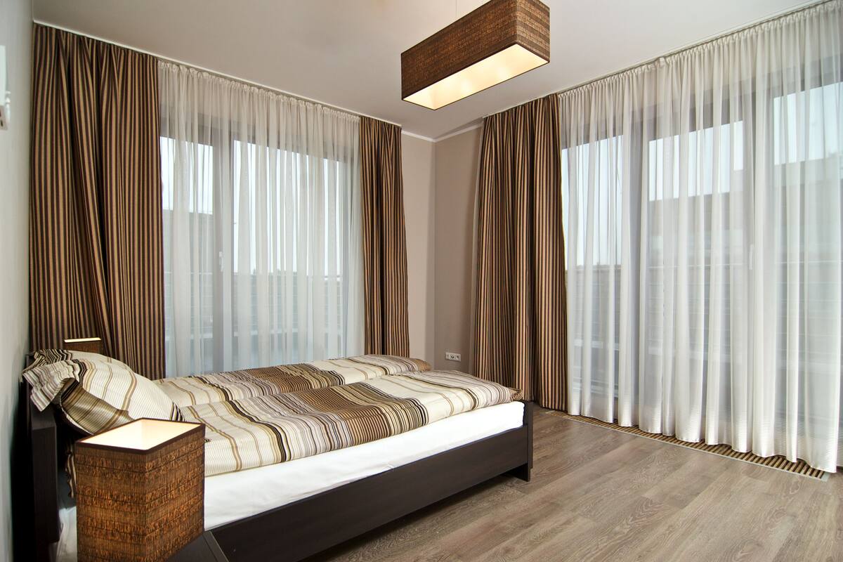 Une chambre moderne avec un grand lit, des rideaux légers et un plancher en bois.