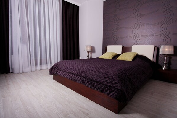 A modern hotel room with a large bed, two bedside lamps, a dark-colored headboard, and a patterned wall.