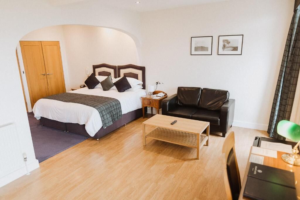 Ein Schlafzimmer mit einem Bett, einem Holztischchen, einer Ledersofa und einem Schreibtisch mit Lampe.
