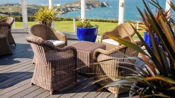 A covered outdoor seating area with wicker furniture and potted plants, overlooking a coastal landscape. - The Atlantic Hotel (Newquay)