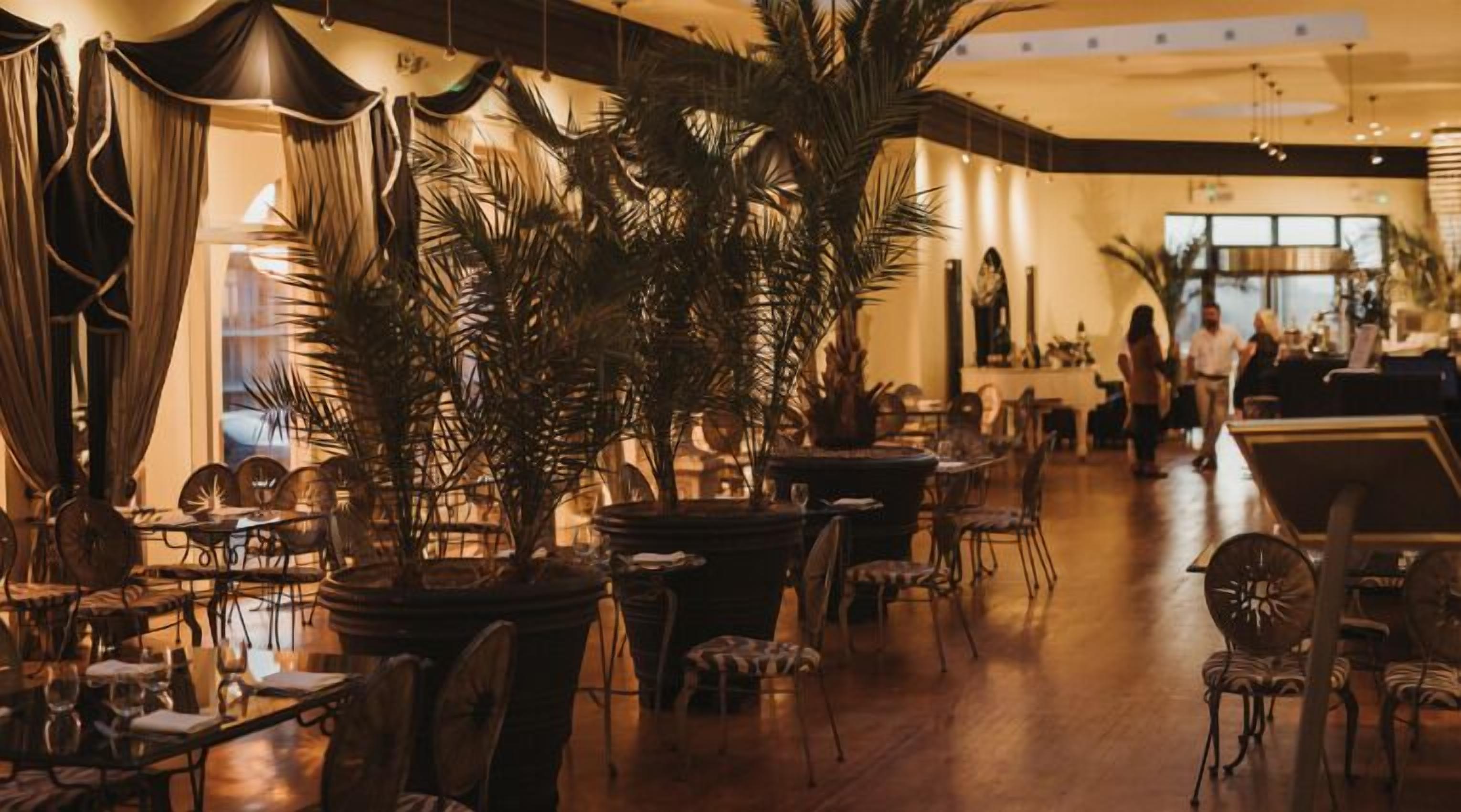 Um restaurante com mesas, cadeiras, plantas em vasos e um balcão comprido.