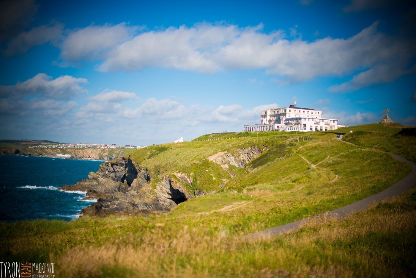 A coastal building with a prominent white facade, situated on a grassy hill overlooking the sea.