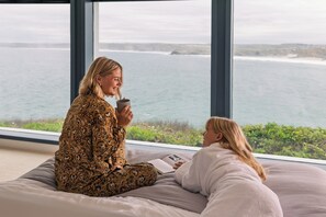 Two individuals seated on a bed with a view of the sea through large windows. - The Atlantic Hotel (Newquay)