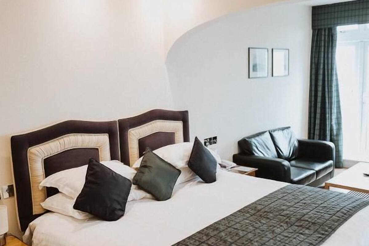 A neatly made bed with a dark headboard, a bedside table, and a black leather chair.