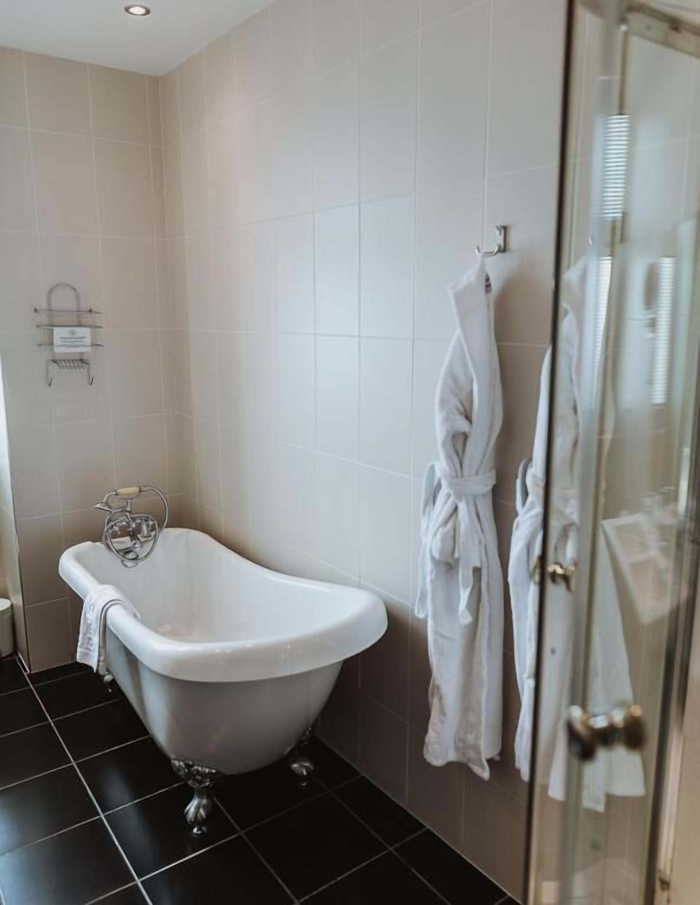 Un baño con una bañera independiente, cabina de ducha de vidrio y un perchero con batas.
