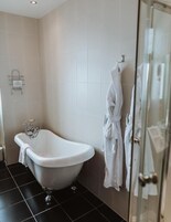 Un baño con una bañera independiente, cabina de ducha de vidrio y un perchero con batas.