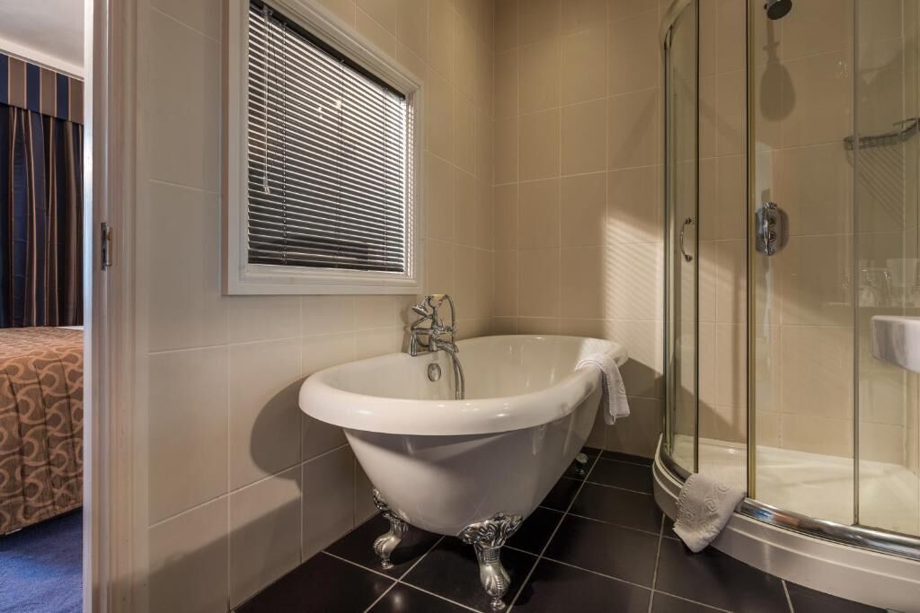 A bathroom with a clawfoot bathtub, a glass shower enclosure, and a window with blinds.